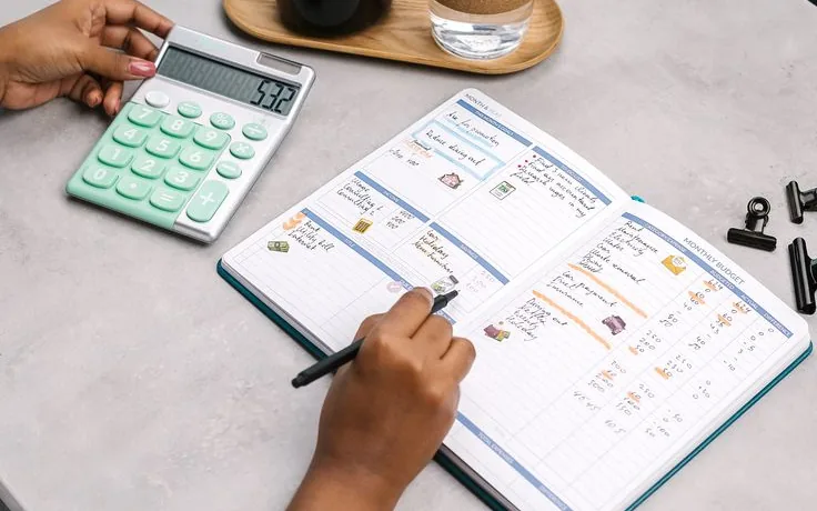 Hands working through a travel budget with a calculator and notebook