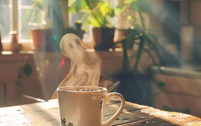 A steaming mug of coffee on a sunlit wooden table by a window
