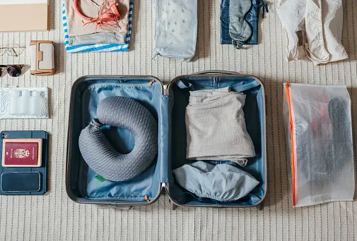 An open suitcase laid flat with travel essentials — passport, sunglasses, packing cubes