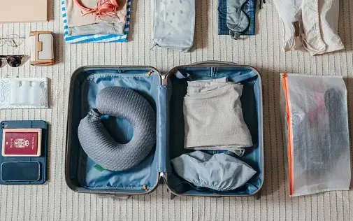 An open suitcase laid flat with travel essentials — passport, sunglasses, packing cubes