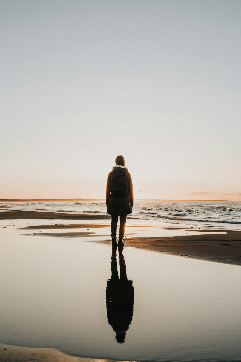 A lone traveler standing at the water's edge, facing the sunset